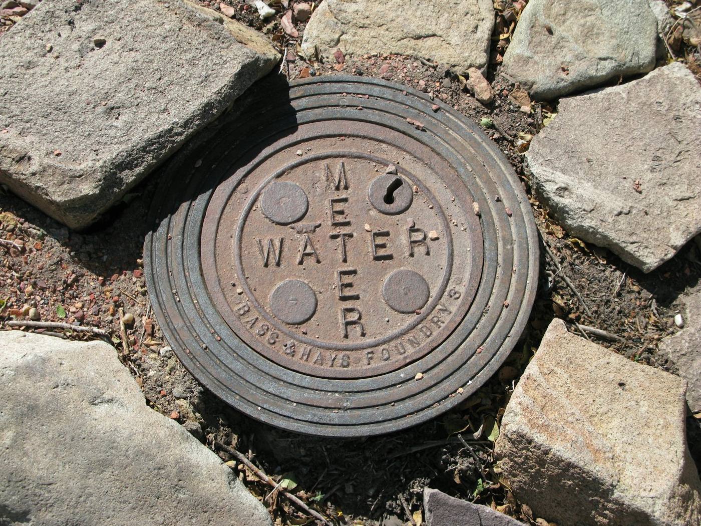 A cast-iron water meter box lid set among stones